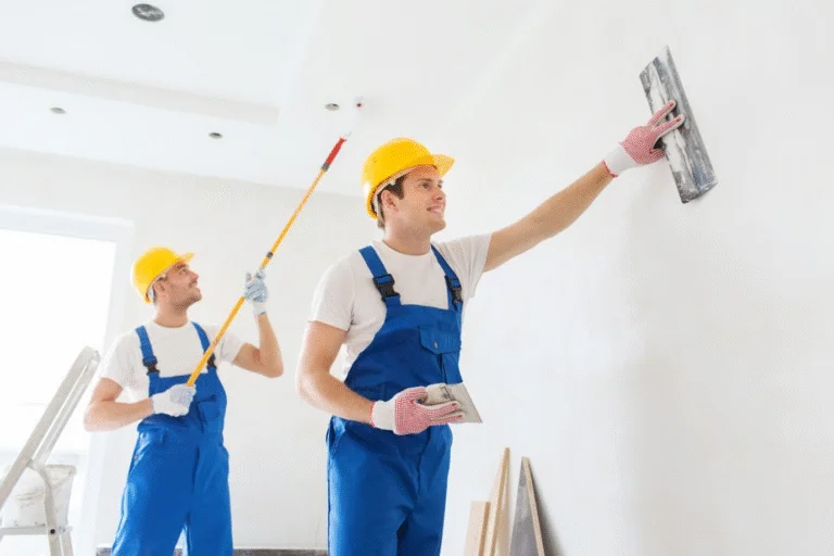 Professional painters in blue uniforms and yellow helmets working on wall painting and plastering service